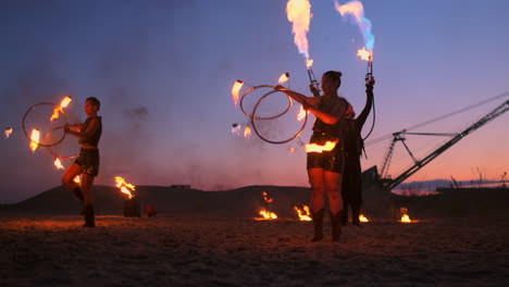 Fire-show-three-women-in-their-hands-twist-burning-spears-and-fans-in-the-sand-with-a-man-with-two-flamethrowers-in-slow-motion